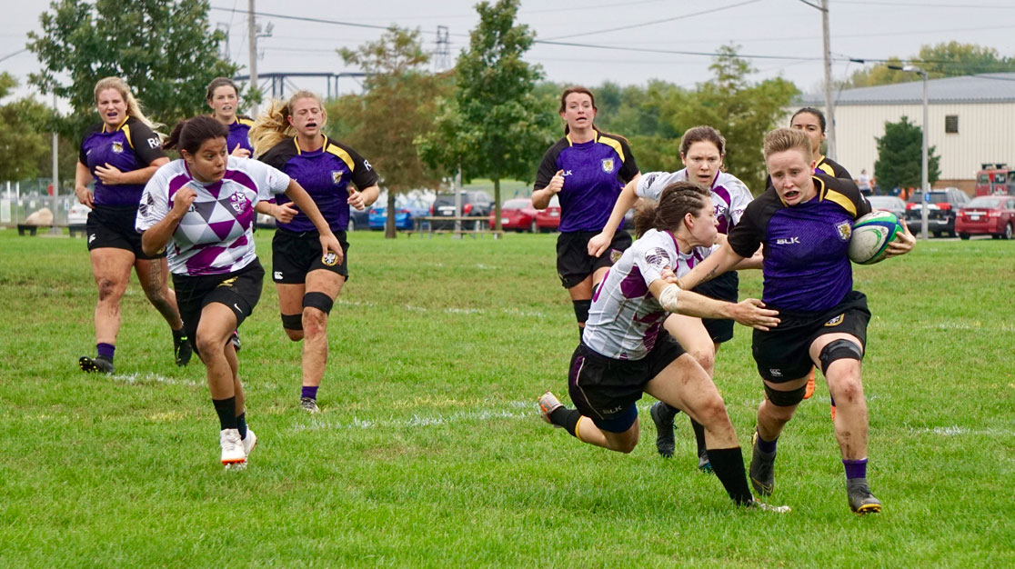 Two teams of women's rugby players running on pitch.