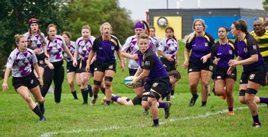 Two teams of women's rugby players running on pitch.