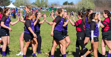 Two women's rugby teams high fiving on grass pitch.