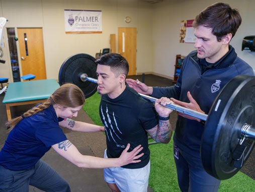 Clinic doctor and student evaluating student's form while lifting.