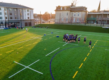 women's rugby players grouped together on large green field.