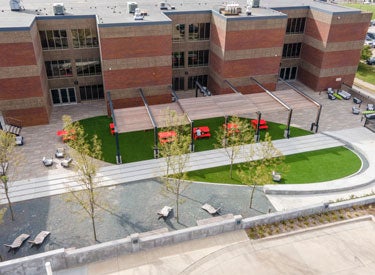 Drone view of large building in background of green area offering seating.