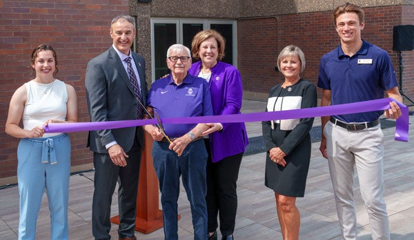 Dr. Kiernan holding large scissors ready to cut purple ribbon at building dedication.