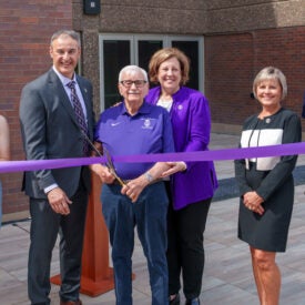 Dr. Kiernan holding large scissors ready to cut purple ribbon at building dedication.