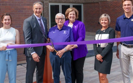 Dr. Kiernan holding large scissors ready to cut purple ribbon at building dedication.