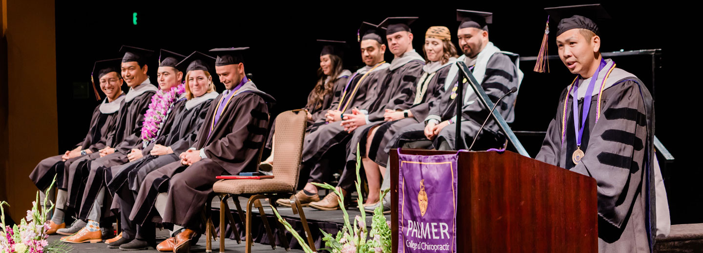 Palmer West graduates in robes sitting on stage.