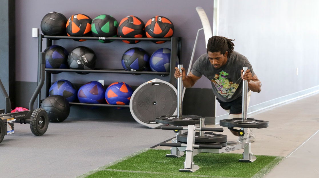 Student using resistance equipment with rack of weight balls in the background.