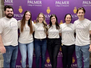 Group of students gathered in Canadian Club shirts in front of Palmer background.