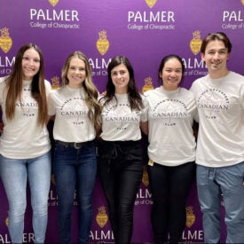 Group of students gathered in Canadian Club shirts in front of Palmer background.