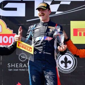 Stephen Hamman smiling and holding racecar trophies.