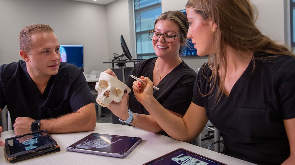 Three students reviewing skeleton models on tablets and