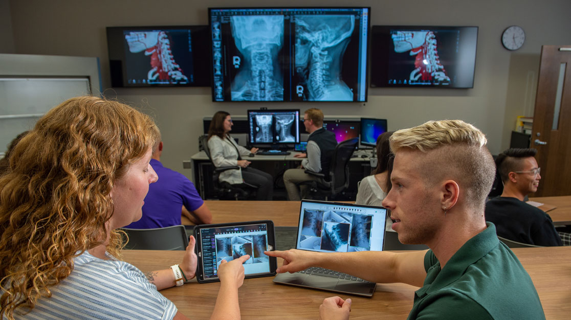 Sets of students reviewing X-rays on large screens and tablets.