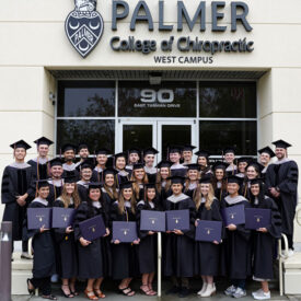 Class 167 graduates in front of West building holding diplomas.