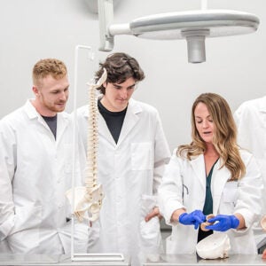 Dr. Kingsley presenting material to two students wearing white lab coats.