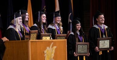 Group of students in graduation cap and gowns holding awards.