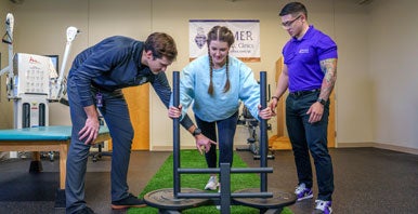 Instructor, intern and student using rehab equipment.