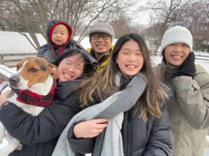 Wu family in snow outfits holding dog. 