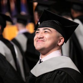 Student smiling wearing graduation cap and gown.