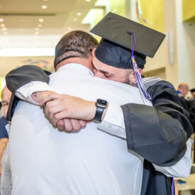 Graduating student in hat and gown hugging a relative.
