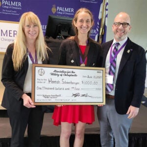 Hannah Schoenberger standing with two faculty members and holding a large check.