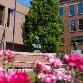 Brick wall with four busts behind pink flowers.