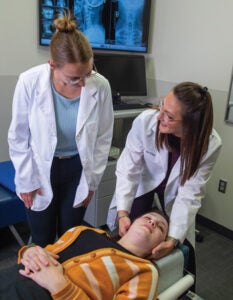 Dr. Asby palpating client's neck while student observes. 