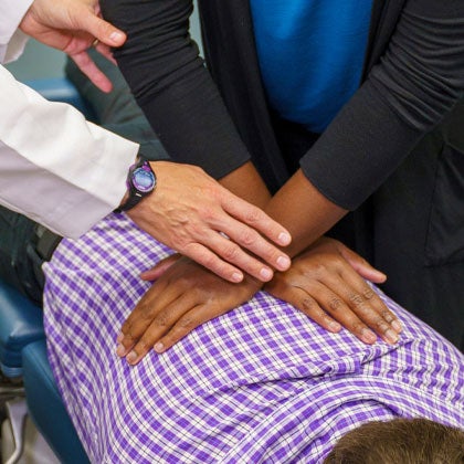 Clinician observing intern's hands on patient's back.