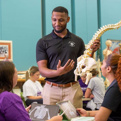 Instructor speaking with students in the library with spine model.