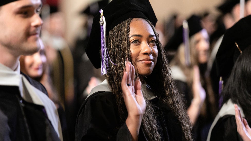 Student in graduation cap and gown with hand up for oath.