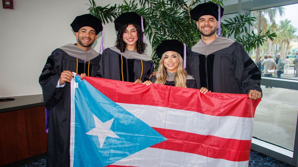 Students in cap and gowns posing with Puerto Rican flag.