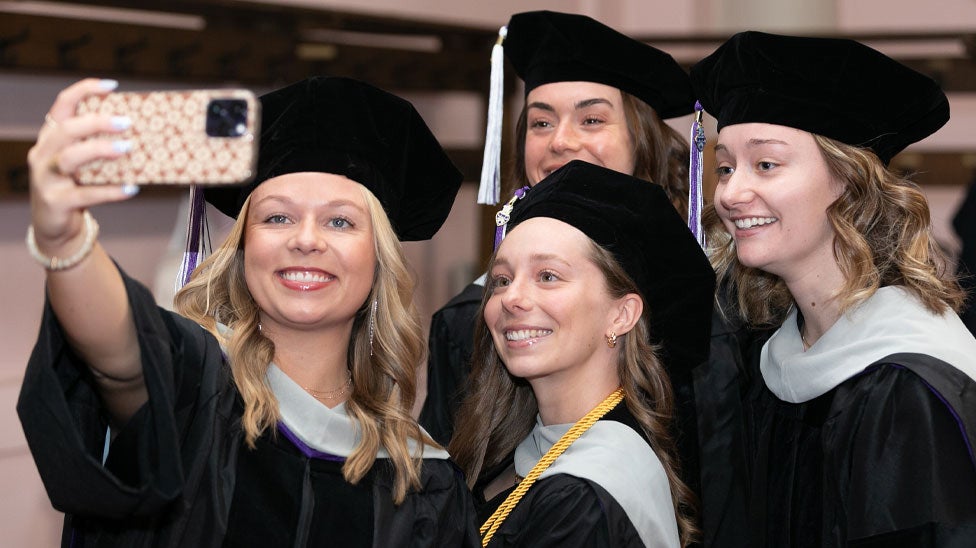 Students in graduation cap and gowns taking selfie.