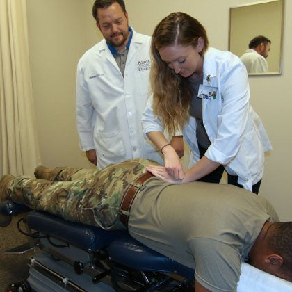Clinician observing student adjusting military member's back.